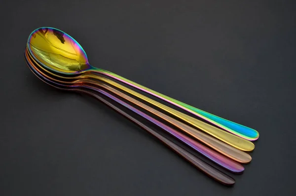 Multicolored table spoons on a plain black background, picture for an article about tableware or cutlery, with a copyspace