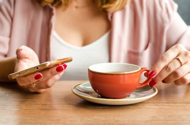 Kırmızı çay fincanı, kafedeki bir masada gri çaydanlık standı. Arka planda, genç bir kadın akıllı telefonu üzerinde çalışıyor.