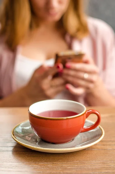 赤いティーカップ 灰色のティーポットはカフェのテーブルの上に立っています 背景には 若い女性がスマートフォンに取り組んでいます — ストック写真