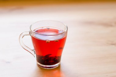 Kafedeki ahşap bir masanın arka planında şeffaf bir fincanda kırmızı çilek çayı.