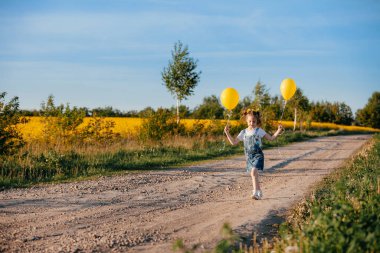Çocuklar güzel bir arazide yürür, sarı bir tarlada çiçek açan kolza tohumlarıyla..