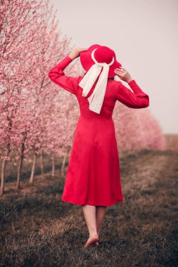 Kırmızı elbiseli ve kırmızı şapkalı bir kadın bahçede yürüyor. Doğada bir yürüyüş. Bahar tatili.