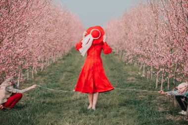 Kırmızı elbiseli ve kırmızı şapkalı bir kadın bahçede yürüyor. Doğada bir yürüyüş. Bahar tatili.