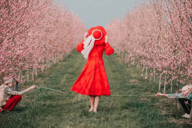 Kırmızı elbiseli ve kırmızı şapkalı bir kadın bahçede yürüyor. Doğada bir yürüyüş. Bahar tatili.