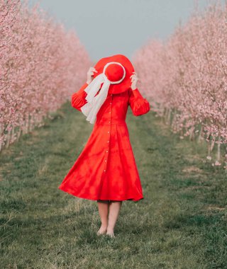 Kırmızı elbiseli ve kırmızı şapkalı bir kadın bahçede yürüyor. Doğada bir yürüyüş. Bahar tatili.