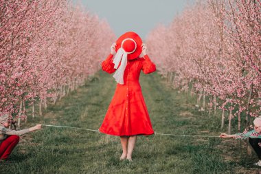 Kırmızı elbiseli ve kırmızı şapkalı bir kadın bahçede yürüyor. Doğada bir yürüyüş. Bahar tatili.