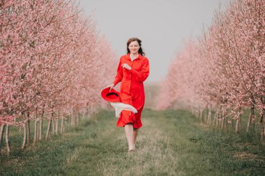 Kırmızı elbiseli ve kırmızı şapkalı bir kadın bahçede yürüyor. Doğada bir yürüyüş. Bahar tatili.