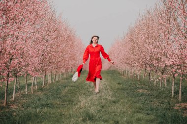 Kırmızı elbiseli ve kırmızı şapkalı bir kadın bahçede yürüyor. Doğada bir yürüyüş. Bahar tatili.