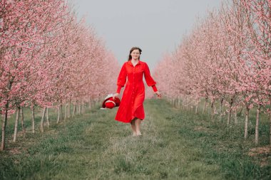 Kırmızı elbiseli ve kırmızı şapkalı bir kadın bahçede yürüyor. Doğada bir yürüyüş. Bahar tatili.