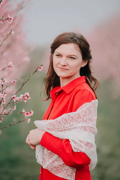 Kırmızı elbiseli ve beyaz pelerinli bir kadın çiçek açan bir bahçede duruyor. Doğada bahar tatili. Keyfin yerinde..