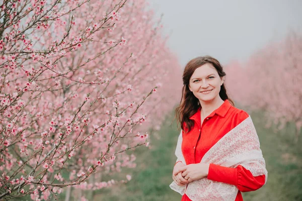 Kırmızı elbiseli ve beyaz pelerinli bir kadın çiçek açan bir bahçede duruyor. Doğada bahar tatili. Keyfin yerinde..