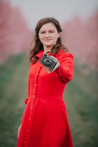 A woman is holding a camera. Photosession. Flowering garden. Spring.
