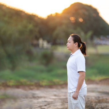 Asyalı uzun saçlı adam altın alacakaranlıkta kuru tarlada duruyor ve dinleniyor..