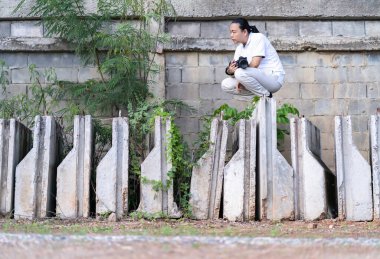 Asyalı profesyonel kameraman oturur ve inşaat alanında ve çevrede nasıl yaratıcılık fotoğrafı oluşturulacağını düşünür..