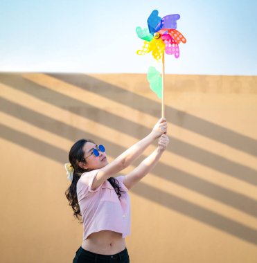 Asyalı kadın, gün batımında çatıda renkli gökkuşağı renginde Windmill Toy oynar ve ilan verir..