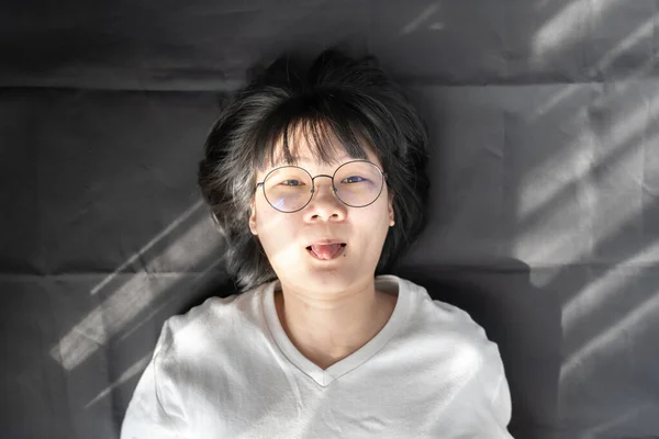 漂亮的短头发眼镜亚洲女人戴在黑色皱纹布的背景上 伸出舌头 — 图库照片