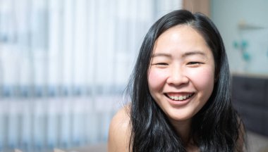 Kendine güvenen Asyalı küçük gözlü kadın yatak odasında gülümsüyor..