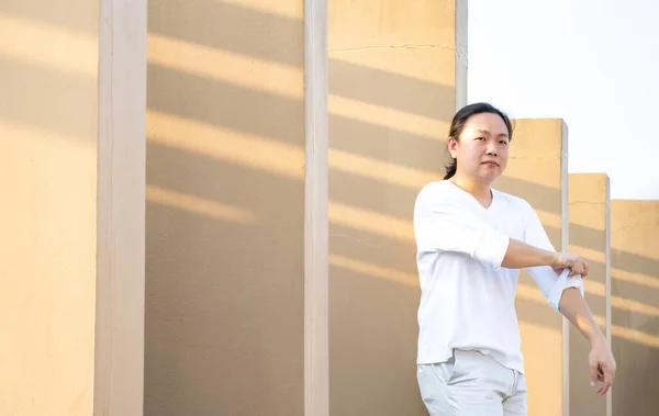亚洲长发 身穿白色长臂T恤衫的男子站在室外的屋顶上 身披浅褐色的墙壁 — 图库照片