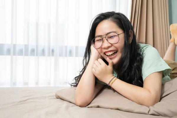 Óculos Bonitos Mulher Asiática Está Rindo Enquanto Deitada Barriga Cama — Fotografia de Stock