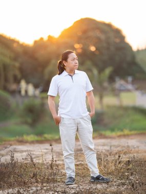 Asyalı uzun saçlı adam altın alacakaranlıkta kuru tarlada duruyor ve dinleniyor..