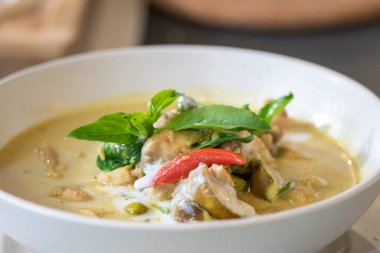 Yeşil Curry 'ye yaklaş, üzerine biber ve fesleğenle süslenmiş tavuk hasırlı krem rengi minder üzerine beyaz kase ile servis edildi..