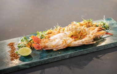 Istakoz Pad Thai, sarı erişte, kızarmış tofu, tere, fasulye filizi, acı biber gücü, sarımsak soğanı ve dikdörtgen bir tabağa konmuş limon ile servis edilir.. 