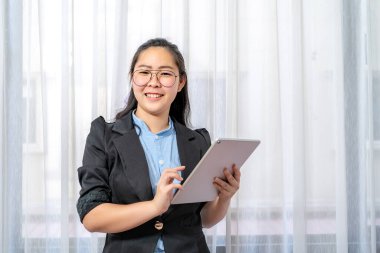 Asyalı bir iş kadını elinde tabletle bürodaki kameraya baktı ve gülümsedi..