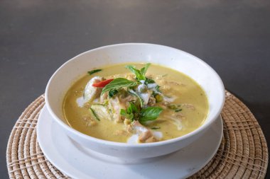 Üzerine biber ve fesleğen ile süslenmiş yeşil körili tavuk hasır krem rengi plasemat ile servis edildi..