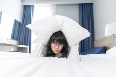 Asyalı güzel gözlüklü kadın korkmuş ve rahatsız hisseder, beyaz yastığı başını yatağa koymak için tutar.