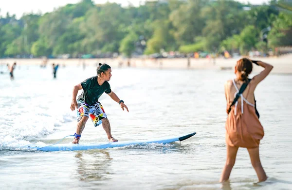 成熟したサーフマンは プーケット県タイのカタビーチで波をサーフィンします ぼやけた女が彼の横で写真を撮っている間 — ストック写真