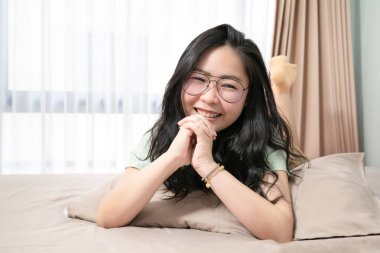 Güzel Asyalı kadın ellerini bir arada tutarken yatak odasında karnının üzerinde uzanırken pastel yeşili, kahverengi temalı.