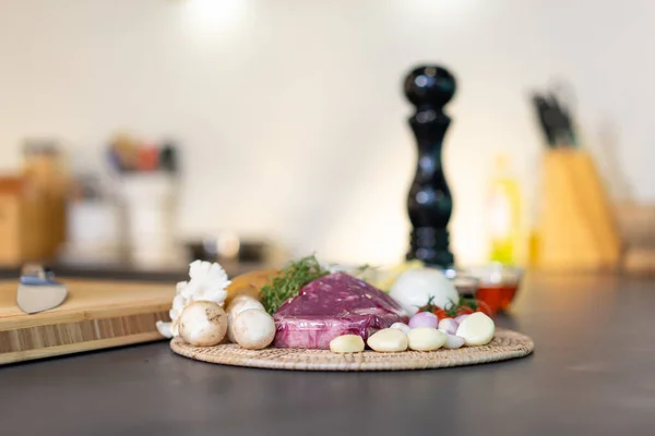 黑花岗岩厨房柜台面上圆形柳条盘中的牛肉牛排和蘑菇酱料菜单原料 — 图库照片