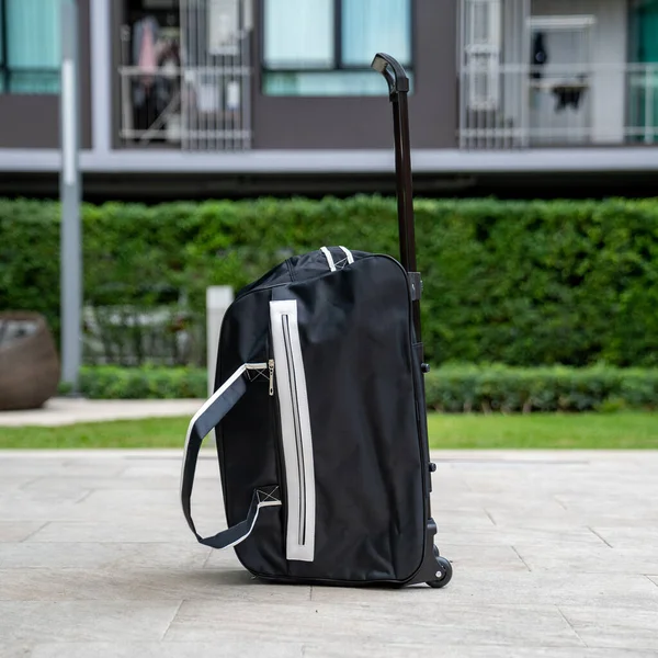 ブッシュを背景にした豪華なマンションの歩道には 車輪付きの旅行者用の黒と白のストライプのスーツケースが残されていました — ストック写真