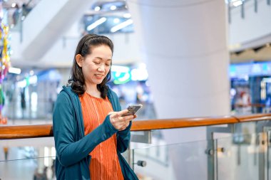 Güzel Asyalı Kadın, Bangkok 'taki mağaza atmosferinde cep telefonu tutuyor ve oynuyor.