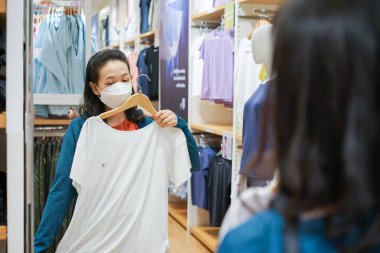 Genç Asyalı Kadın Kumaş Moda Dükkanı 'nda aynanın önünde T-Shirt' ü dene..