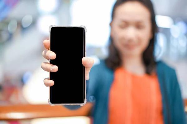 Black screen of mobile in Asian woman hand with blur face in department store background. For mock up website or application on smart phone. Clipping Path.