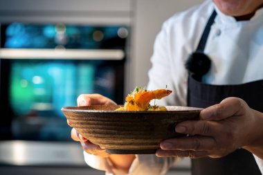 Şefin eli, pişmiş karidesi fırının arka planında bulanık bir şekilde kasede tutuyor..