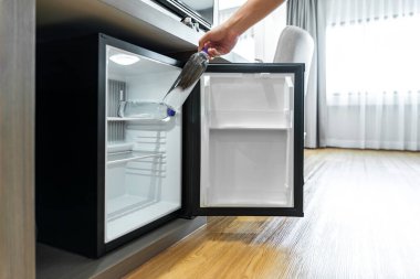 Man Hand küçük bir buzdolabı açtı ve otel odasındaki ahşap tezgahın altındaki plastik su şişesine ulaştı..