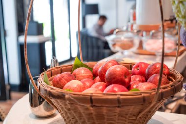 Meyve sepetindeki kırmızı elmalar biraz bulanık arka planda, sanki bir otelin yemek odasındaymışlar gibi..