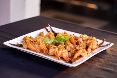 Demirhindi soslu çıtır karidesler beyaz kare tabakta, üzerine jöle serpiştirilmiş ve üstü kızarmış arpacık soğanı ve kişniş. Çıtır çıtır, baharatlı ve tatlı tatların mükemmel dengesi var..