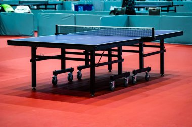 Blue table tennis or pingpong table is settle on a red, orange floor of the indoor court stadium for competitions tournament.