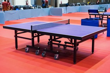 Blue table tennis or pingpong table is settle on a red, orange floor of the indoor court stadium for competitions tournament.