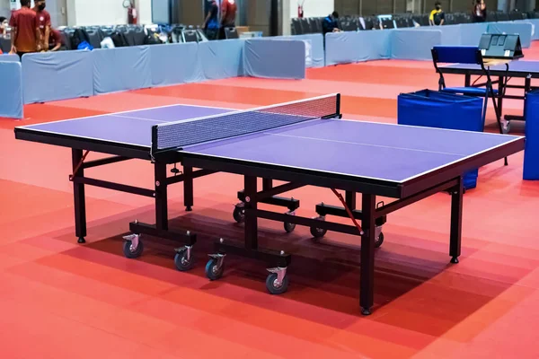 Blue table tennis or pingpong table is settle on a red, orange floor of the indoor court stadium for competitions tournament.