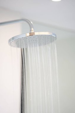 Water was pouring out from a large circular shower in the dimly lit bathroom that has a glass window and can see the view outside.