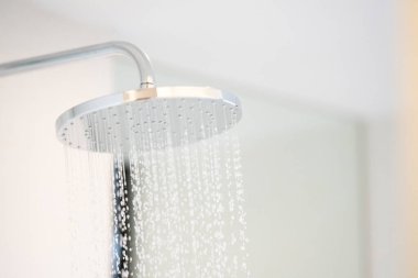 Water was pouring out from a large circular shower in the dimly lit bathroom that has a glass window and can see the view outside.