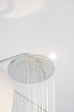 Water was pouring out from a large circular shower in the dimly lit bathroom that has a glass window and can see the view outside.