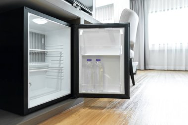 Otel odasındaki ahşap tezgahın altında küçük siyah buzdolabı.