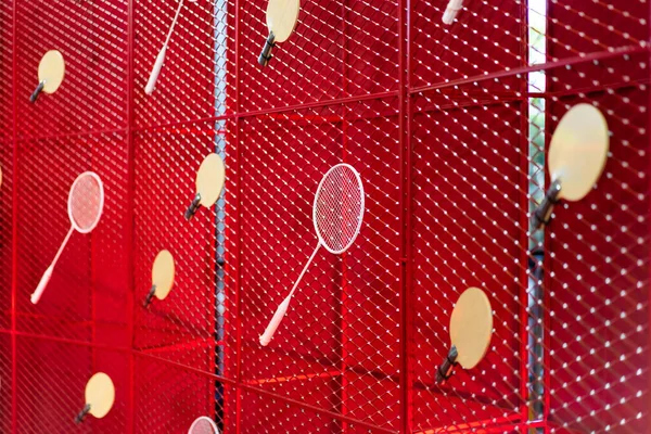 Table tennis and badminton rackets are hung on a red square grill steel grid, used as a backdrop for various events.