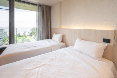 2 single beds with white bedding are in the cream bedroom of hotel that turn on the headboard light and open the gray curtain.