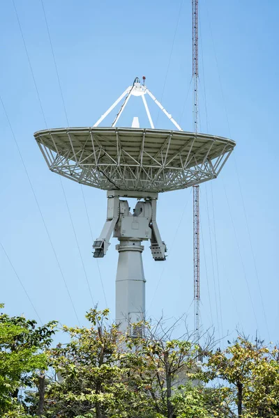 stock image parabolic antenna satellite dish located in front of telecommunication tower with a clear blue sky in the background.